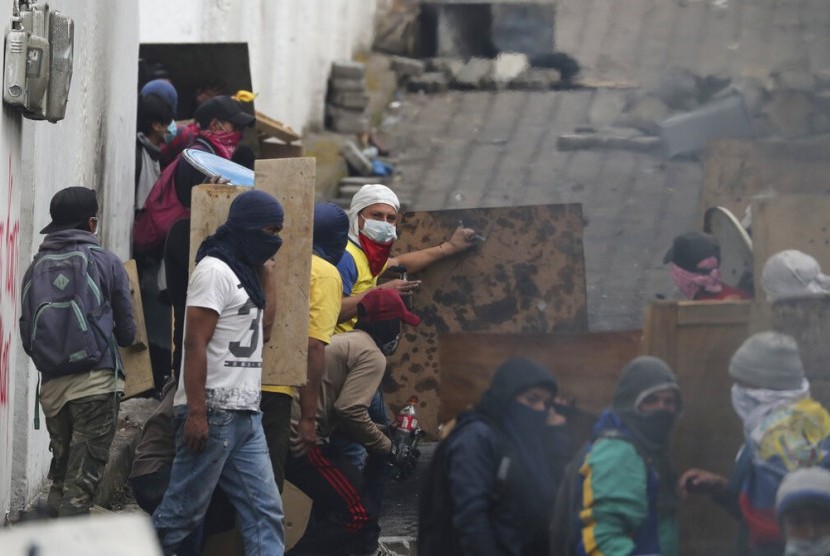 Pengunjuk rasa antipemerintah berlindung di balik perisai kayu saat bentrok dengan polisi di dekat Dewan Nasional saat penerapan jam malam di Quito, Ekuador, Ahad (13/10).