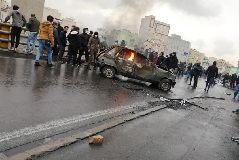 Pengunjuk rasa Iran berdiri di sekitar kendaraan dibakar selama bentrokan menyusul kenaikan harga bahan bakar di Teheran, Iran.