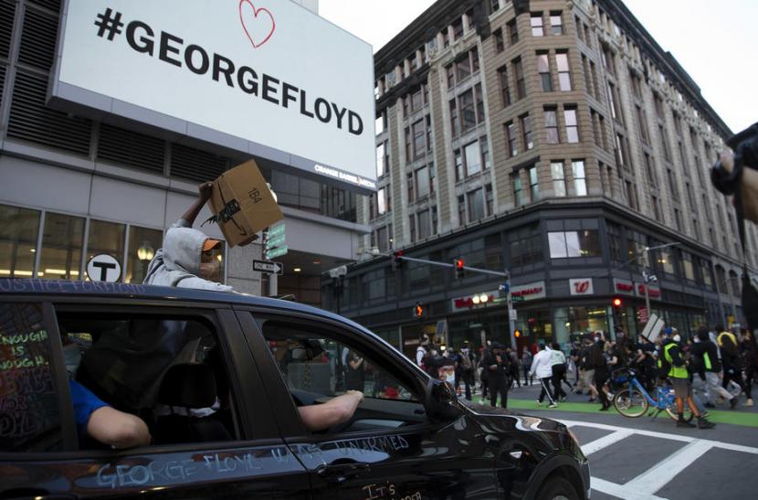 Pengunjuk rasa melewati papan bertuliskan #GEORGEFLOYD di Boston, Amerika, (31/5), sebagai bentuk simpati terhadap tragedi kemanusiaan yang menimpa George Floyd yang tewas di tangan polisi.