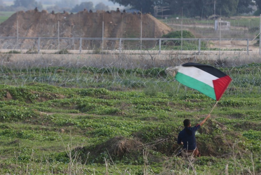 Pengunjuk rasa mengibarkan bendera Palestina di depan tentara Israel setelah terjadi bentrokan di dekat perbatasan Israel dan Jalur Gaza, (20/11).