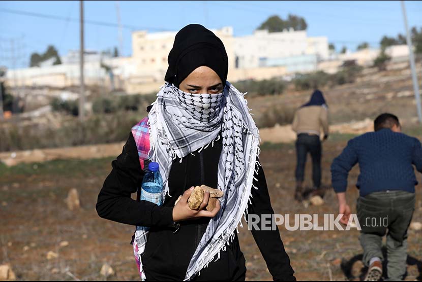 Pengunjukrasa wanita membawa batu di Kota Ramallah, Tepi Barat, Palestina, Jumat (8/12)
