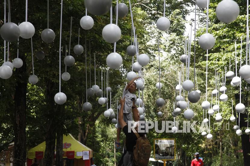 Pengunjung melintas di bawah dekorasi berbahan bola plastik di Taman Satwa Taru Jurug (TSTJ) Solo, Jawa Tengah, Rabu (29/12/2021). Selain sebagai daya tarik wisata bagi pengunjung, dekorasi tersebut dibuat untuk memeriahkan dan mendukung timnas sepak bola Indonesia pada ajang final Piala AFF 2020 di Singapura. 