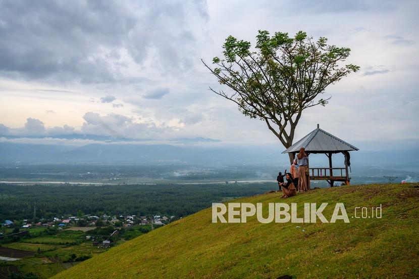 Pengunjung menikmati pemandangan dari puncak saat berwisata di Bukit Satu Pohon, Sulawesi Tengah. Jelang akhir tahun pemerintah diminta membuat kebijakan yang tidak sebabkan lonjakan kasus Covid-19.