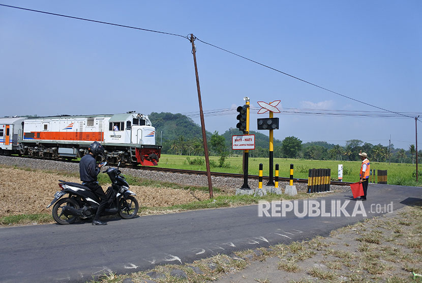 Penjaga perlintasan menghentikan kendaraan ketika sebuah kereta api melintas di perlintasan kereta api tanpa palang pintu di Desa Bedadung, Pakusari, Jember, Jawa Timur, Selasa (5/6). 