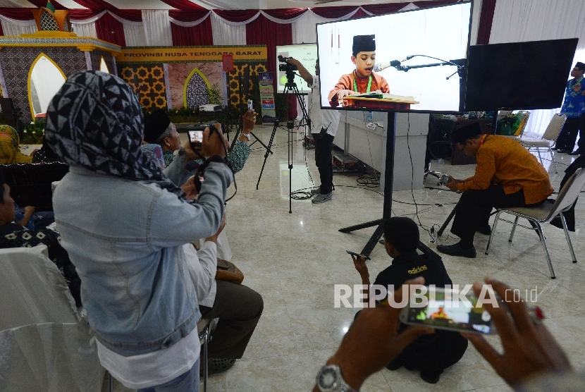 Penonton mengabadikan kafilah yang membacakan ayat suci Al Quran melalui layar saat menjalani sesi final lomba tartil Al Quran dalam rangkaian MTQ Nasional ke XXVI yang diadakan di Aula Rinjani Gedung BKD, Kota Mataram, Nusa Tenggara Barat, Jumat (5/8). 