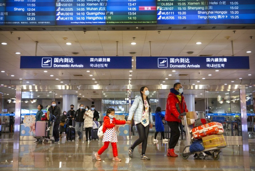 Penumpang pesawat mengenakan masker melewati papan pengumuman menunjukkan pembatalan penerbangan dari Wuhan di Bandara Beijing, Kamis (23/1). Pemerintah menutup akses ke kota Wuhan yang berpenduduk 11 juta jiwa akibat virus korona. 