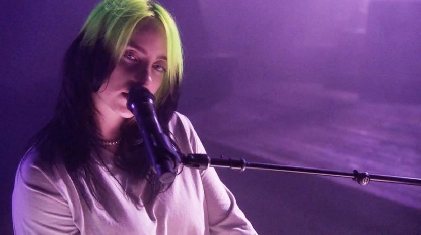 Penyanyi Billie Eilish mempertahankan gaya khasnya, setelan baju longgar serta rambut hitam dengan semburat hijau neon yang ikonik, dalam video klip lagu terbarunya. 