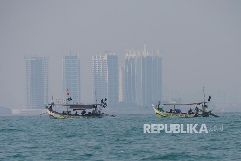Perahu nelayan berlayar di perairan Teluk Jakarta dengan latar kabut asap polusi yang menyelimuti Kota Jakarta.