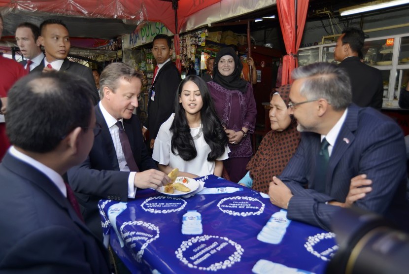 Perdana Menteri Inggris David Cameron (kedua kiri) didampingi Dubes Inggris untuk Indonesia Moazzam Malik (kanan) dan artis Maudy Ayunda (tengah) menikmati pisang goreng di warung halaman Masjid Agung Sunda Kelapa, Jakarta, Selasa (28/7).