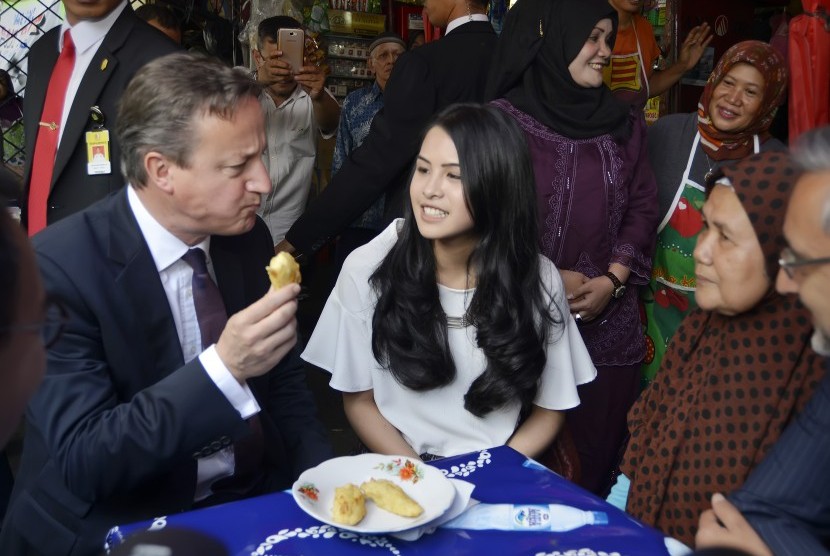 Perdana Menteri Inggris David Cameron (kiri) didampingi Dubes Inggris untuk Indonesia Moazzam Malik (kanan) dan artis Maudy Ayunda (kedua kiri) menikmati pisang goreng di warung halaman Masjid Agung Sunda Kelapa, Jakarta, Selasa (28/7).