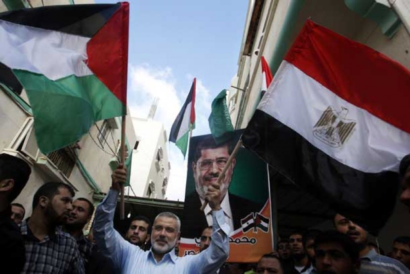  Perdana Menteri Palestina Ismail Haniyeh memegang bendera Palestina dan Mesir dengan latar belakang poster presiden Mesir terpilih Muhammad Mursi di Gaza, Palestina.