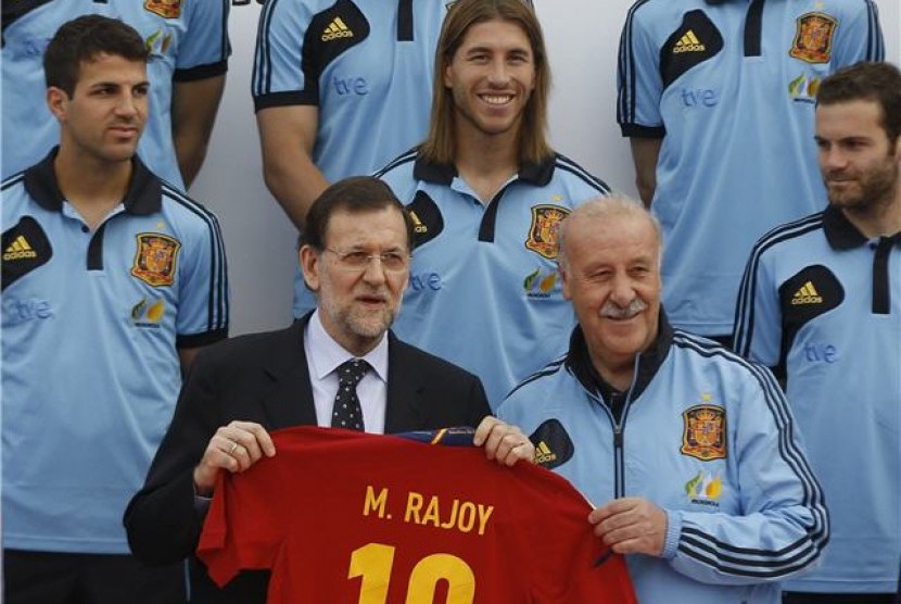 Perdana Menteri Spanyol, Mariano Rajoy (tengah), memegang replika jersey timnas Spanyol atas nama dirinya saat mengujungi pemusatan pelatihan timnas di Las Rozas, Madrid, pada Jumat (1/6). 