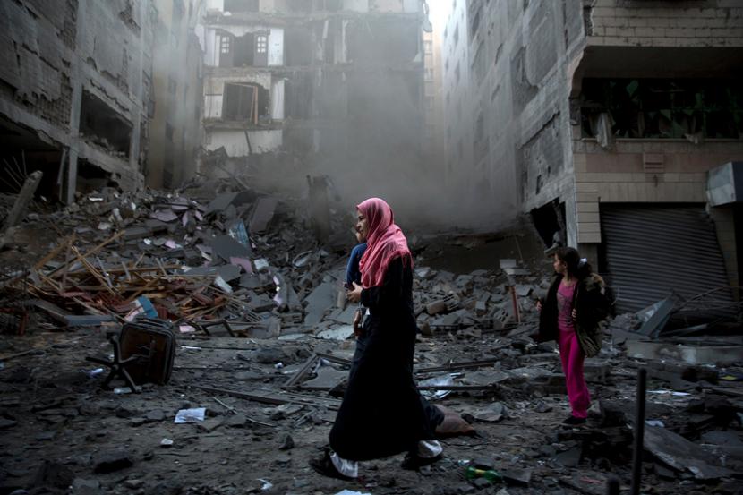 Perempuan dan anaknya melintasi puing reruntuhan bangunan di Gaza yang hancur karena serangan bom Israel.