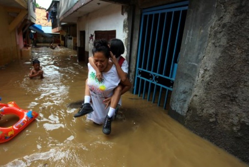 [ilustrasi] Perempuan menggendong seorang anak saat berjalan menembus banjir yang menggenangi kawasan Kampung Pulo di Jakarta, Senin (16/11)