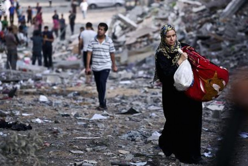 Perempuan Palestina membawa barang di tengah reruntuhan gedung di Jalur Gaza.