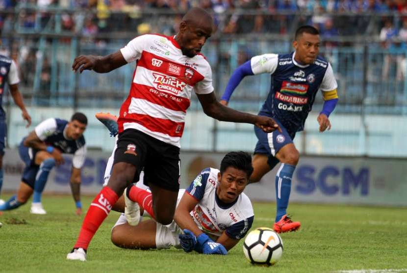 Pesepak bola Madura United, Greg Nwokolo (kiri), lolos dari adangan panjaga gawang Arema FC, Utam Rusdiana (bawah), dalam pertandingan Liga I di Stadion Kanjuruhan, Malang, Jawa Timur, Senin (17/9).