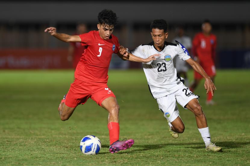 Pesepak bola Singapura U19 Ilyasin Zayan (kiri) berebut bola dengan pesepak bola Timor Leste U19 Cristevao Moniz Fernandes (kanan) dalam laga penyisihan grup Piala AFF U19 di Stadion Madya Senayan, Jakarta, Selasa (5/7/2022). 