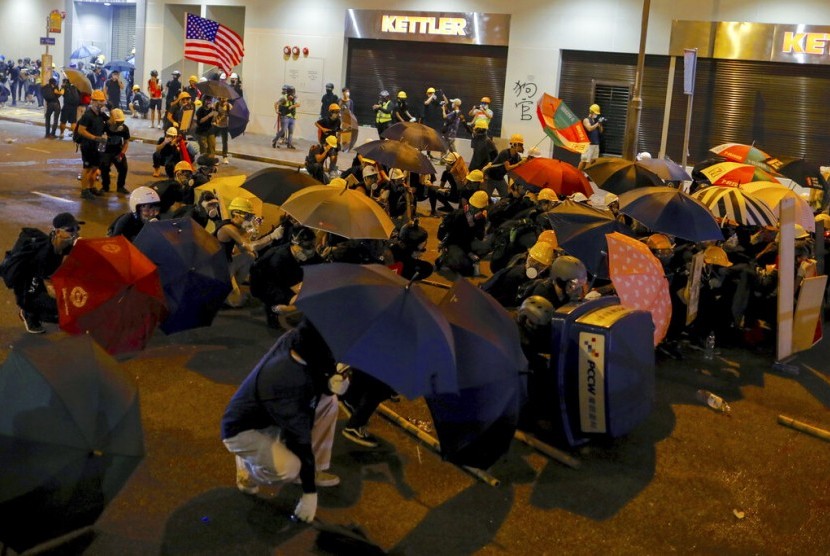 Peserta aksi melindungi diri mereka dengan payung dari semprotan gas air mata yang dilancarkan petugas di Hong Kong, ahad (28/7).