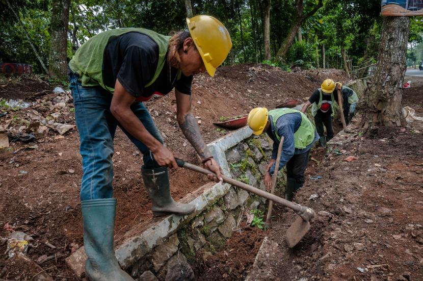 Peserta program padat karya membersihkan rumput di bahu jalan. 