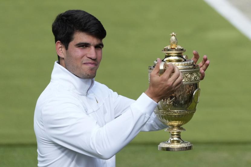 Petenis Spanyol Carlos Alcaraz memegang trofi juara tunggal putra Grand Slam Wimbledon 2024. 