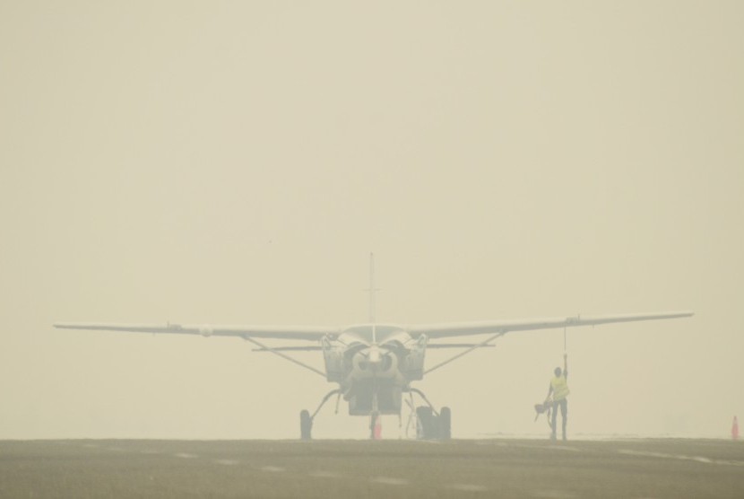 Petugas Apron Movement Control (AMC) Bandara Sultan Thaha Jambi mengecek kondisi pesawat Susi Air jenis Caravan C.208B yang diparkir di landasan yang diselimuti kabut asap di Jambi, Kamis (3/9). 