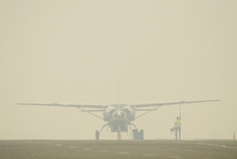 Petugas Apron Movement Control (AMC) Bandara Sultan Thaha Jambi mengecek kondisi pesawat Susi Air jenis Caravan C.208B yang diparkir di landasan yang diselimuti kabut asap di Jambi.