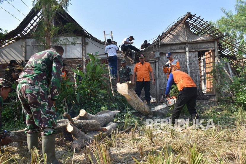 Prajurit TNI, petugas BPBD, Polri, dan warga membersihkan pohon tumbang yang menimpa rumah penduduk akibat puting beliung. 