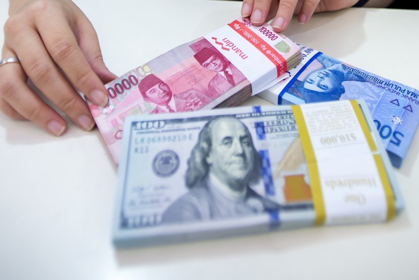 Petugas Bank Mandiri menunjukkan pecahan uang rupiah dan dollar Amerika Serikat.