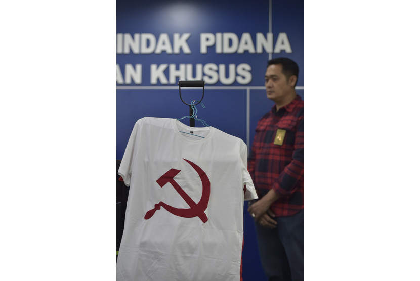 Petugas berdiri di dekat barang bukti berupa kaus berlambang palu arit saat rilis penangkapan tersangka penjual kaus berlogo palu arit melalu media daring di Bareskrim Polri, Jakarta, Jumat (30/12). 