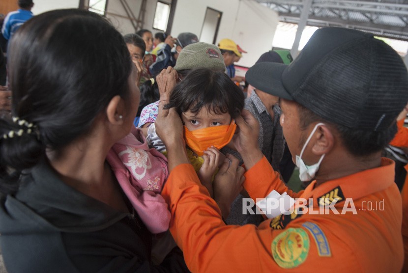 Petugas BPBD memasangkan masker kepada seorang anak pengungsi Gunung Agung di lokasi penampungan Desa Bebandem, Karangasem, Bali, Ahad (26/11).