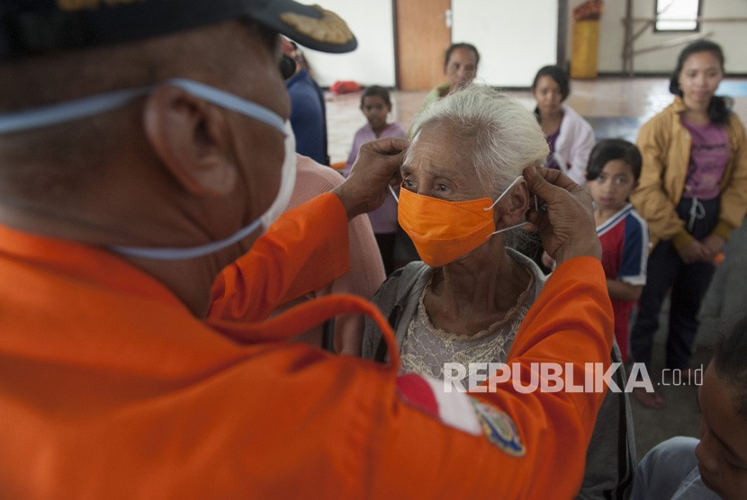 Petugas BPBD memasangkan masker pada seorang pengungsi  (ilustrasi)