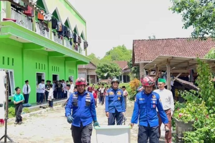 Petugas damkar berjalan sambil menjinjing kotak berisi ular piton dan membawanya keluar dari lingkungan pondok pesantren Darissulaimaniyah di Kecamatan Durenan, Trenggalek, Selasa (9/1/2024). 