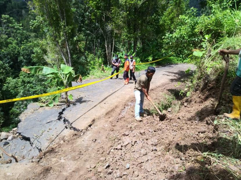 Petugas dan warga membersihkan sisa material di jalan penghubung Tasikmalaya-Pangandaran, yang tergerus longsor di Desa Cisarua, Kecamatan Cineam, Kabupaten Tasikmalaya, Sabtu (11/4).