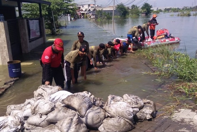 Petugas dari Pemkot Surabaya mengangkut handbag menggunakan perahu boat untuk menutup tanggul Anak Kali Lamong yang jebol di RW 03, Kelurahan Sumberejo, Kecamatan Pakal, Kota Surabaya, Jumat (3/5).