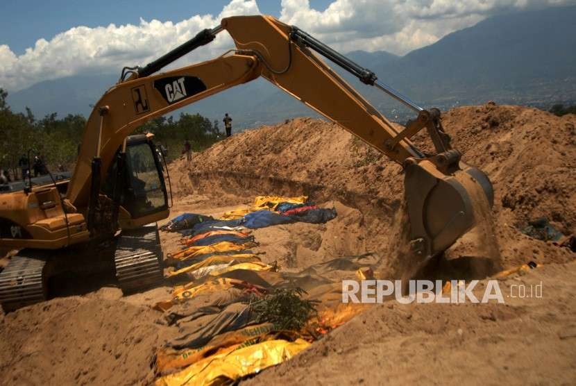 Petugas dengan alat berat mengubur jenazah korban gempa Palu di TPU Poboya Indah, Palu, Sulawesi Tengah, Selasa (2/10).