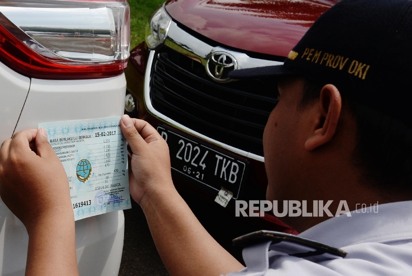 Petugas Dinas Perhubungan dan Transportasi DKI Jakarta menempelkan stiker seusai memeriksa kendaraan roda empat saat uji KIR khusus kendaraan sewa berbasis transportasi online di Silang Monas, Jakarta, Senin (15/8). (Republika/ Yasin Habibi)