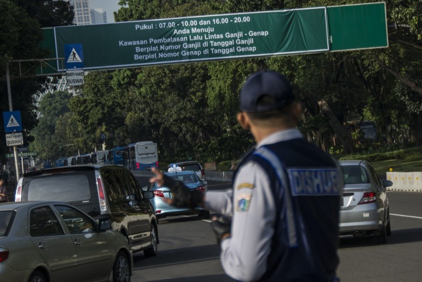 Petugas Dinas Perhubungan mengatur arus lalu lintas saat uji coba penerapan sistem lalu lintas pelat ganjil-genap di Jalan Medan Merdeka Barat, Jakarta, Rabu (27/7).