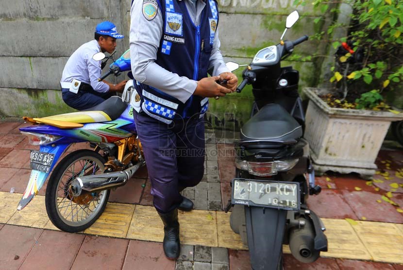   Petugas Dishub DKI mencabut pentil ban motor dan mobil yang parkir sembarangan di Jalan Matraman, Jakarta Timur, Senin (10/3).   (Republika/Yasin Habibi)