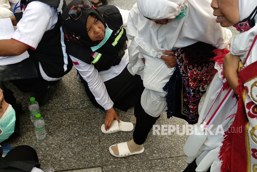 Petugas haji Indonesia memakaikan sandal pada jamaah yang kehilangan di Gerbang 21 Masjid Nabawi, Jumat (27/7). Tim kesehatan membagikan ribuan sandal mengingat berbahayanya berjalan-jalan tanpa sandal di tengah cuaca panas Madinah.