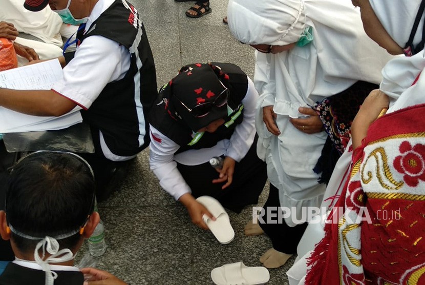 Petugas haji Indonesia memakaikan sandal pada jamaah yang kehilangan di Gerbang 21 Masjid Nabawi. Madinah Lebih Panas Dibanding Makkah, Jamaah Jangan Sampai Kehilangan Alas Kaki
