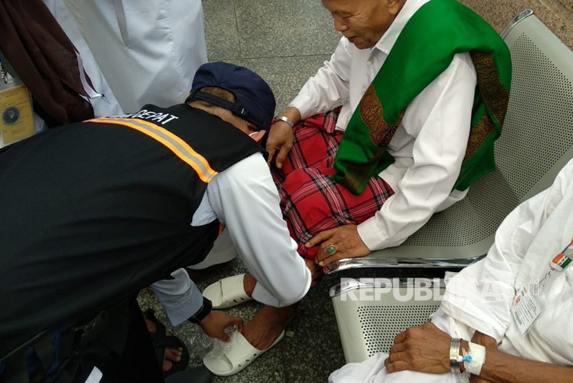 Petugas haji Indonesia memakaikan sandal pada jamaah yang kehilangan di Gerbang 21 Masjid Nabawi, Jumat (27/7). Tim kesehatan membagikan ribuan sandal mengingat berbahayanya berjalan-jalan tanpa sandal di tengah cuaca panas Madinah.