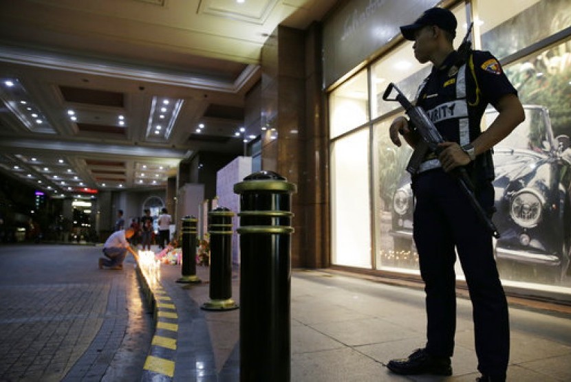 Petugas keamanan berjaga saat seorang pria menyalakan lilin bagi korban di kasino komplek Resorts World Manila, Jumat (2/6) di Manila, Filipina. 
