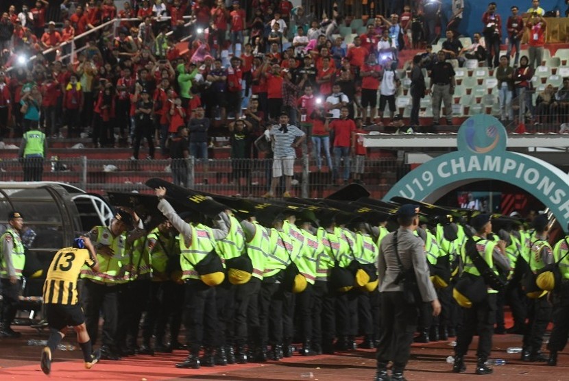 Petugas keamanan berusaha melindungi pesepak bola Malaysia U19 Mohamad Izzuddin (kiri) dari lemparan suporter Indonesia usai laga semi final Piala AFF U19 di Gelora Delta Sidoarjo, Sidoarjo, Jawa Timur, Kamis (12/7). Indonesia kalah adu pinalti dengan Malaysia dengan skor 3-4