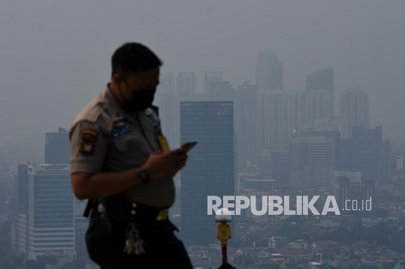 Petugas keamanan memainkan gawainya dengan latar belakang gedung bertingkat di Jakarta, Jumat (8/10/2021). Pemerintah Provinsi DKI Jakarta menargetkan penurunan emisi Gas Rumah Kaca (GRK) sebesar 35 juta ton karbon dioksida ekuivalen (CO2e) pada 2030 melalui sejumlah aksi mitigasi mulai dari sektor energi hingga pengolahan limbah.