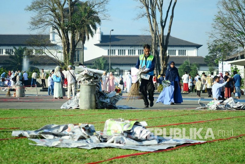 Petugas kebersihan membersihkan alas koran bekas Shalat Id, di Lapangan Gasibu, Kota Bandung, Sabtu (25/6).