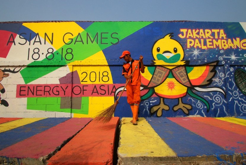 Petugas kebersihan menyapu dengan latar belakang mural Asian Games 2018 di Kampung Tematik, Kemayoran, Jakarta, Sabtu (21/7). 