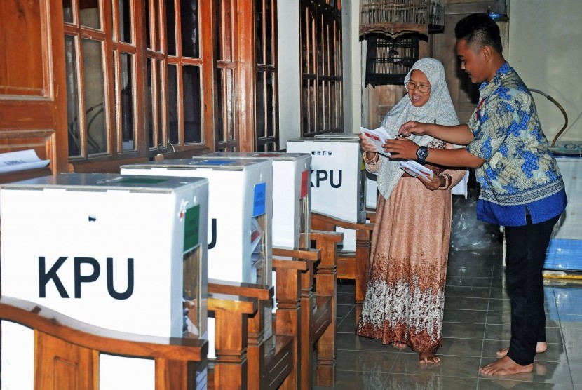 Petugas Kelompok Penyelenggara Pemungutan Suara (KPPS) membantu warga memasukkan surat suara kedalam kotak suara saat pemungutan suara ulang.