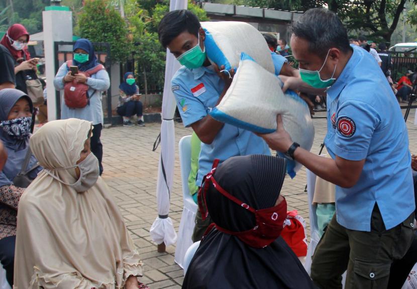 Di tengah suasana pandemi sembari mengenakan masker, petugas Kemensos memberikan beras kepada warga penerima paket sembako bantuan pemerintah tahap lima kepada warga di Rawa Buntu, Tangerang Selatan, Banten.