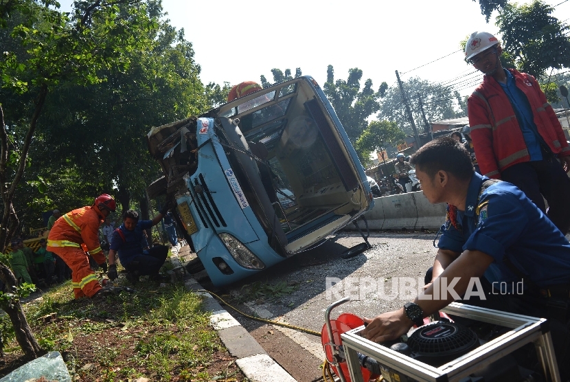  Petugas kepolisian dibantu oleh petugas pemadam kebakaran mengevakuasi bangkai bus Transjakarta yang terbalik saat mengalami kecelakaan di Jalan Warung Buncit, Jakarata Selatan, Rabu (7/6). (Republika/Raisan Al Farisi)