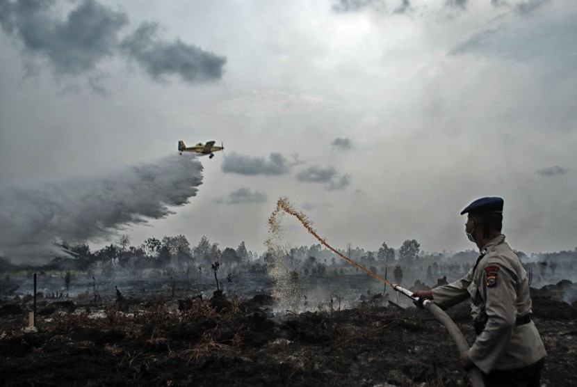 Petugas Kepolisian dibantu pesawat Air Tractor BNPB melakukan pemadaman kebakaran lahan gambut yang terjadi di Desa Rimbo Panjang, Kampar, Riau, Senin (29/8). 